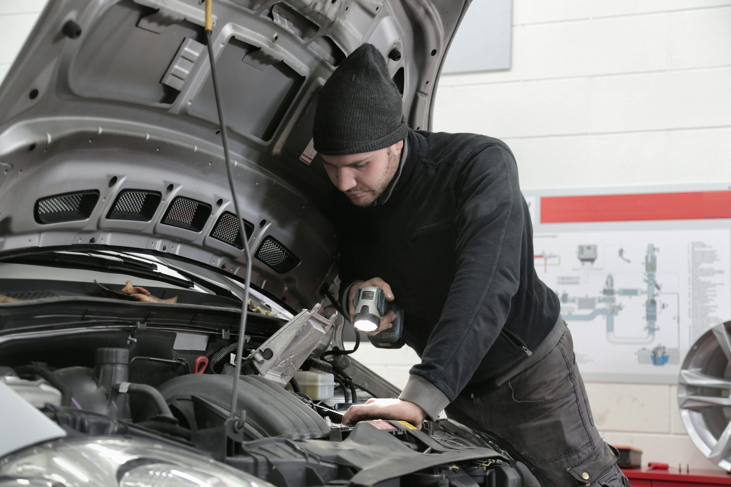 A mechanic closely inspects a car engine in a garage using a flashlight, ensuring proper maintenance.